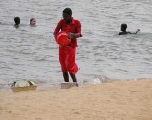 A woman doing dishes at the beach, with Jolie and some other children playing in the water